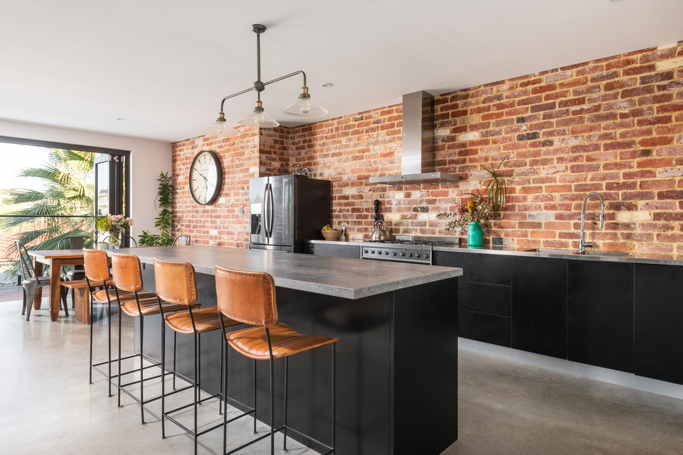 Photo of a mid-sized industrial galley eat-in kitchen in Perth with concrete floors, an integrated sink, flat-panel cabinets, black cabinets, concrete benchtops, red splashback, brick splashback, stainless steel appliances, with island, grey floor and grey benchtop.