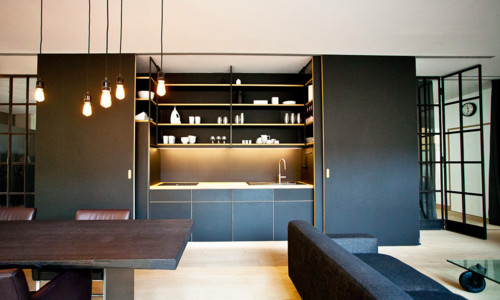 Concealed kitchen with matte black slab kitchen cabinet wall, pocket doors, open shelves, and warm integrated LED lighting