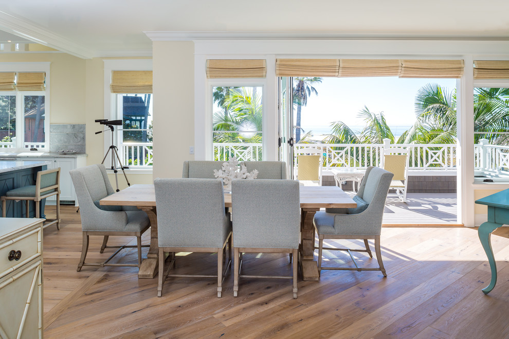 This is an example of a mid-sized beach style open plan dining in San Diego with light hardwood floors, yellow walls, no fireplace and beige floor.