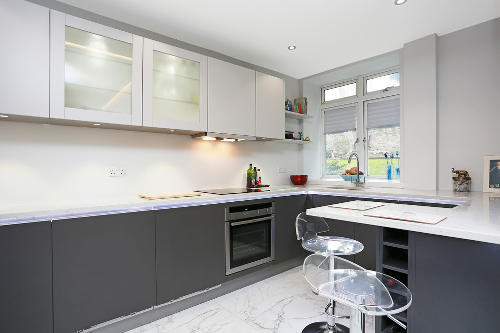 This is an example of a small modern kitchen in London with flat-panel cabinets, stainless steel appliances and a peninsula.