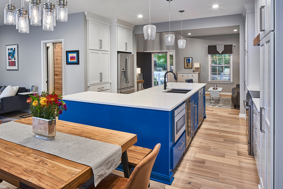Inspiration for a mid-sized eclectic eat-in kitchen in Charlotte with an undermount sink, shaker cabinets, blue cabinets, quartz benchtops, multi-coloured splashback, mosaic tile splashback, stainless steel appliances, light hardwood floors, with island, brown floor and white benchtop.