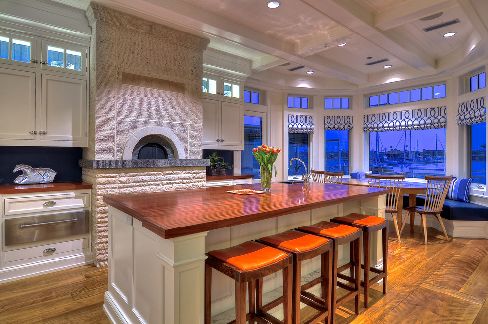 Photo of an expansive traditional single-wall open plan kitchen in Los Angeles with medium hardwood floors, a farmhouse sink, beaded inset cabinets, white cabinets, wood benchtops, stainless steel appliances and multiple islands.