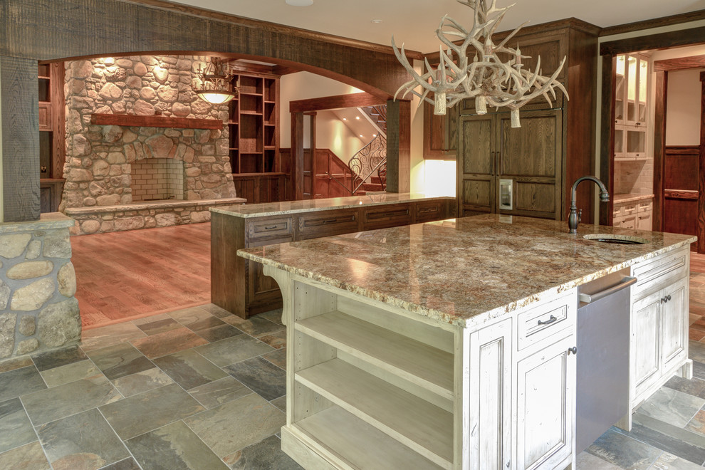 Inspiration for a large rustic l-shaped slate floor and gray floor enclosed kitchen remodel with an undermount sink, recessed-panel cabinets, dark wood cabinets, granite countertops, beige backsplash, stone tile backsplash, paneled appliances, a peninsula and brown countertops