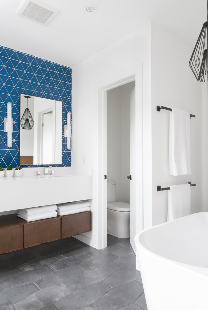 This is an example of a large modern master bathroom in Toronto with flat-panel cabinets, medium wood cabinets, a freestanding tub, a double shower, a two-piece toilet, blue tile, subway tile, white walls, porcelain floors, an undermount sink, marble benchtops, multi-coloured floor, an open shower and white benchtops.