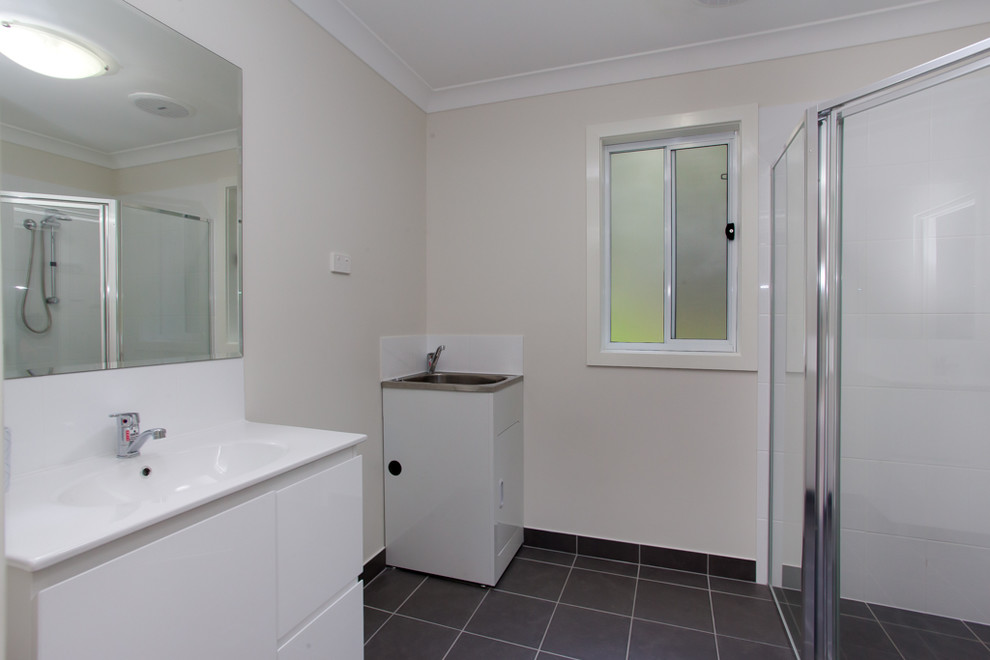 Design ideas for a mid-sized industrial bathroom in Newcastle - Maitland with raised-panel cabinets, white cabinets, a corner shower, a one-piece toilet, white tile, ceramic tile, beige walls, ceramic floors, a drop-in sink, solid surface benchtops, brown floor and a hinged shower door.
