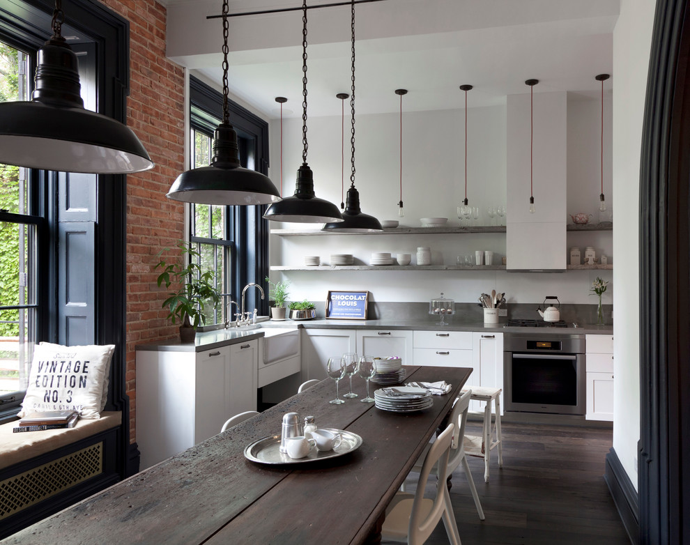 Photo of an industrial eat-in kitchen in New York with a farmhouse sink, shaker cabinets, white cabinets, stainless steel appliances, dark hardwood floors, no island and concrete benchtops.