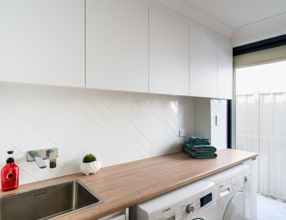 Photo of a small contemporary galley dedicated laundry room in Perth with a drop-in sink, flat-panel cabinets, white cabinets, laminate benchtops, white splashback, ceramic splashback, white walls, ceramic floors, a side-by-side washer and dryer, brown floor and brown benchtop.