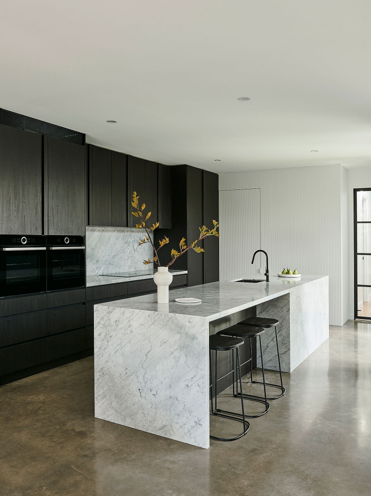 Inspiration for a mid-sized modern galley concrete floor and gray floor eat-in kitchen remodel in Geelong with flat-panel cabinets, black cabinets, quartz countertops, gray backsplash, quartz backsplash, black appliances, an island, black countertops and an undermount sink