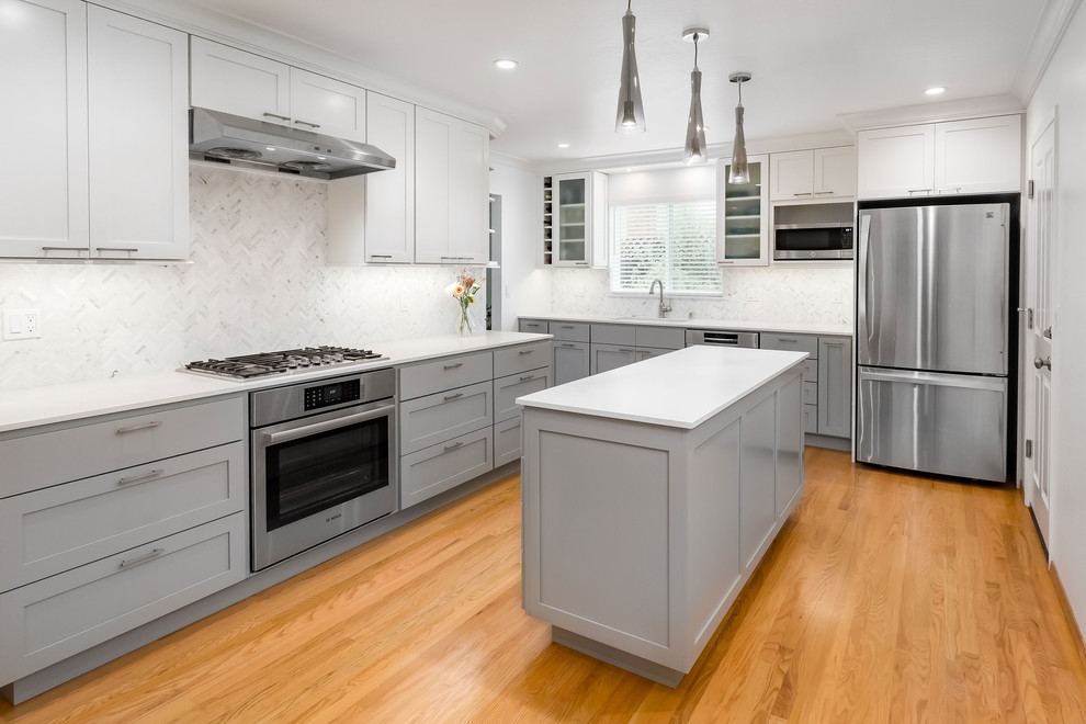This is an example of a large contemporary l-shaped eat-in kitchen in Other with a double-bowl sink, shaker cabinets, white cabinets, quartz benchtops, white splashback, mosaic tile splashback, stainless steel appliances, light hardwood floors and with island.