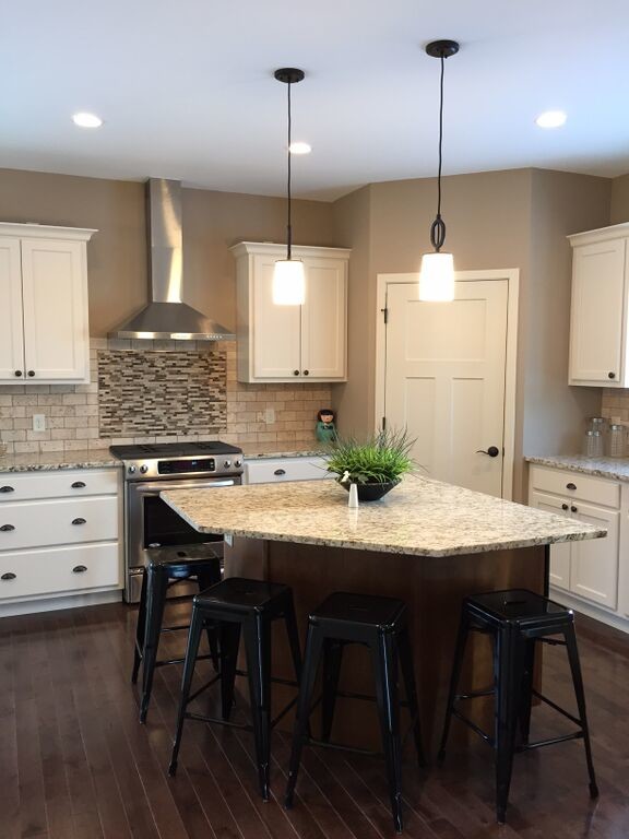 Mid-sized transitional l-shaped dark wood floor eat-in kitchen photo with recessed-panel cabinets, white cabinets, granite countertops, beige backsplash, stone tile backsplash, stainless steel appliances and an island