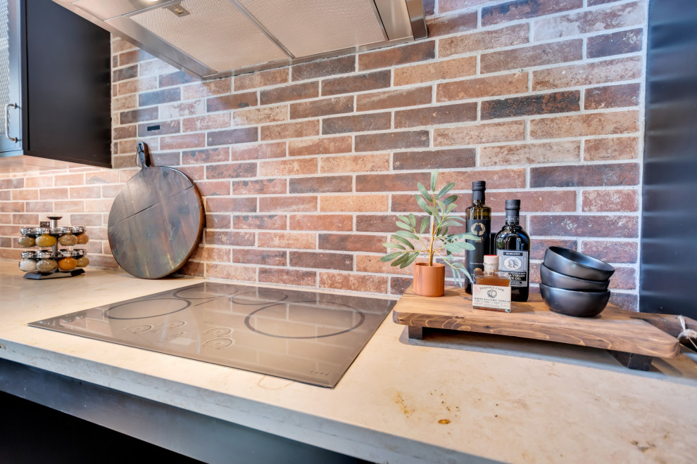 Inspiration for a large industrial l-shaped open plan kitchen in Phoenix with a farmhouse sink, black cabinets, limestone benchtops, multi-coloured splashback, stone tile splashback, stainless steel appliances, porcelain floors, with island, grey floor, beige benchtop and exposed beam.