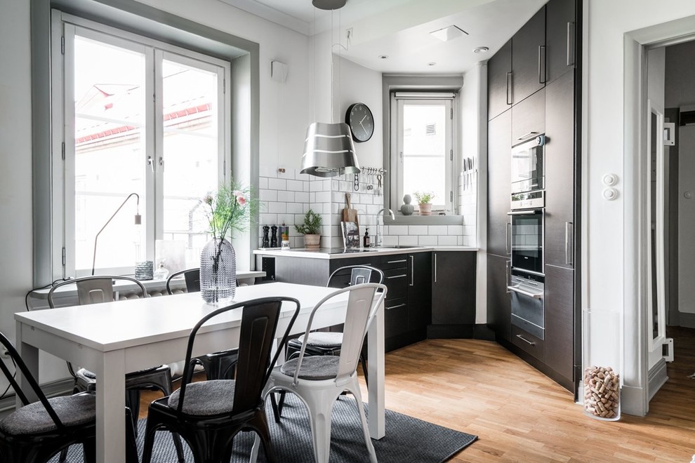 Design ideas for a mid-sized scandinavian kitchen in Gothenburg with flat-panel cabinets, white splashback, subway tile splashback, medium hardwood floors, brown floor and black cabinets.