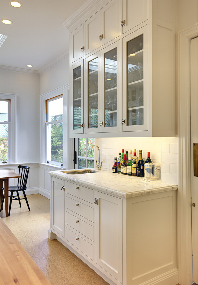 Design ideas for a large traditional l-shaped eat-in kitchen in San Francisco with subway tile splashback, an undermount sink, glass-front cabinets, white cabinets, white splashback, marble benchtops, cork floors, stainless steel appliances and with island.