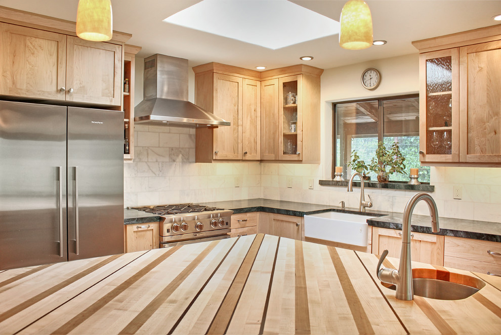 Mid-sized transitional l-shaped light wood floor and brown floor eat-in kitchen photo with a farmhouse sink, shaker cabinets, light wood cabinets, wood countertops, white backsplash, marble backsplash, stainless steel appliances and an island