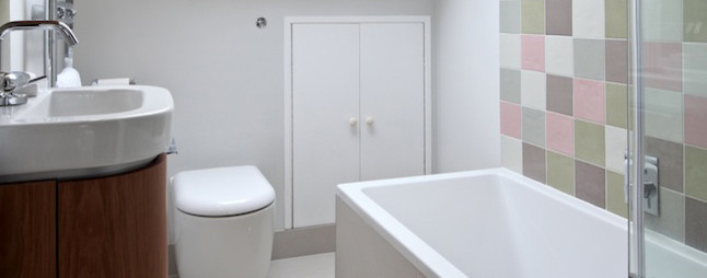 This is an example of a medium sized contemporary ensuite bathroom in London with flat-panel cabinets, medium wood cabinets, a built-in bath, a shower/bath combination, a one-piece toilet, multi-coloured tiles, glass sheet walls, green walls, ceramic flooring, an integrated sink and wooden worktops.