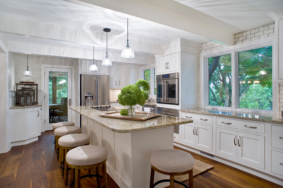 Mid-sized transitional l-shaped medium tone wood floor and brown floor eat-in kitchen photo with an undermount sink, recessed-panel cabinets, white cabinets, granite countertops, white backsplash, subway tile backsplash, stainless steel appliances and an island