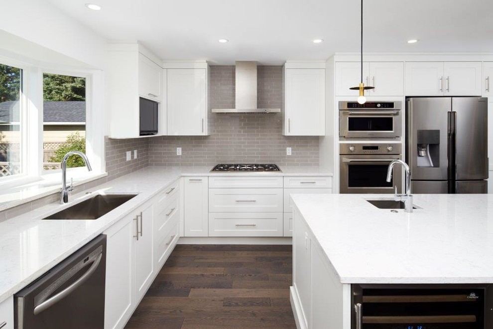 Example of a mid-sized transitional l-shaped dark wood floor and brown floor open concept kitchen design in Calgary with an undermount sink, shaker cabinets, white cabinets, quartz countertops, gray backsplash, subway tile backsplash, stainless steel appliances and an island