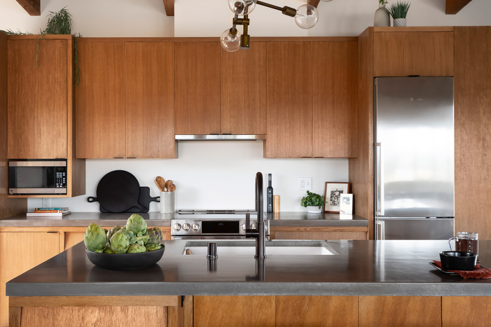 Modern inredning av ett stort grå grått kök, med en enkel diskho, skåp i mellenmörkt trä, bänkskiva i betong, rostfria vitvaror, mellanmörkt trägolv, en köksö och brunt golv