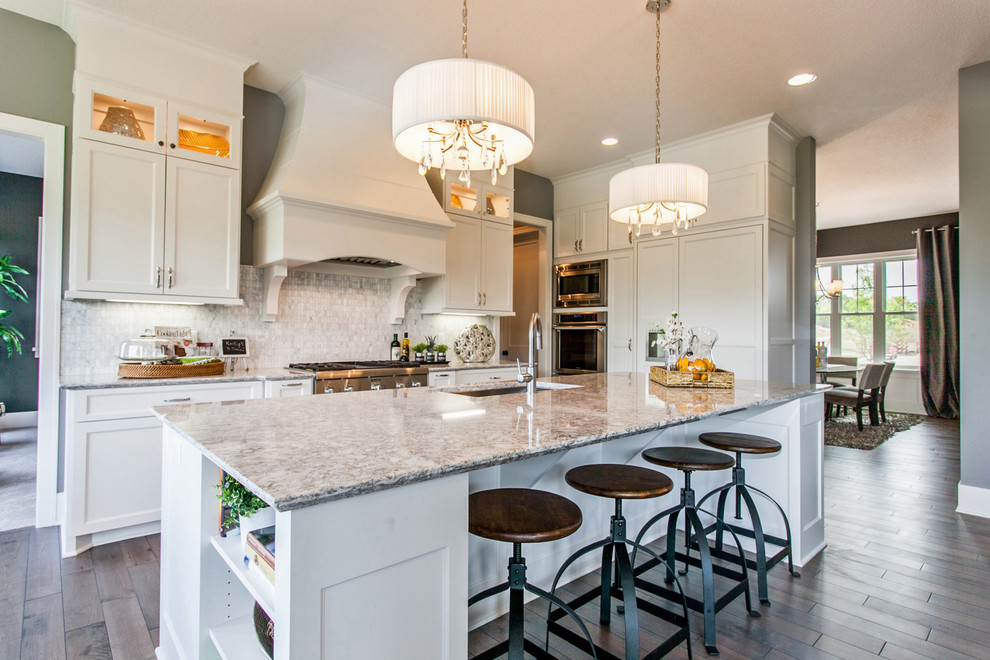 This is an example of a transitional galley kitchen in Minneapolis with an undermount sink, shaker cabinets, white cabinets, grey splashback, stone tile splashback, stainless steel appliances, dark hardwood floors and with island.
