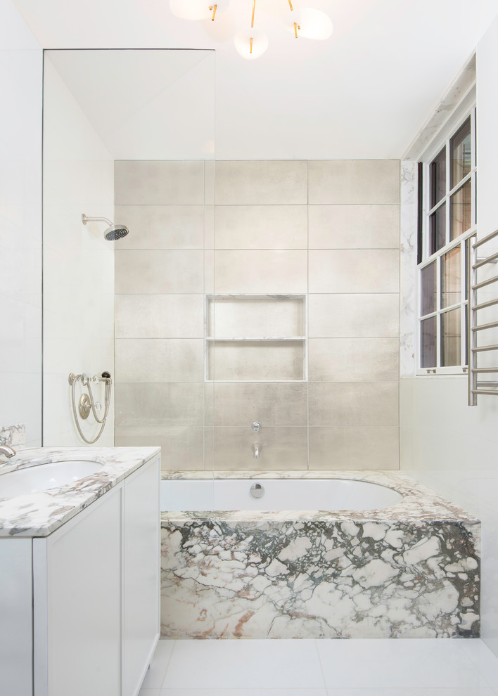 Mid-sized contemporary master bathroom in New York with raised-panel cabinets, white cabinets, a drop-in tub, a shower/bathtub combo, a wall-mount toilet, porcelain tile, white walls, ceramic floors, a drop-in sink, marble benchtops, white floor, an open shower and grey benchtops.