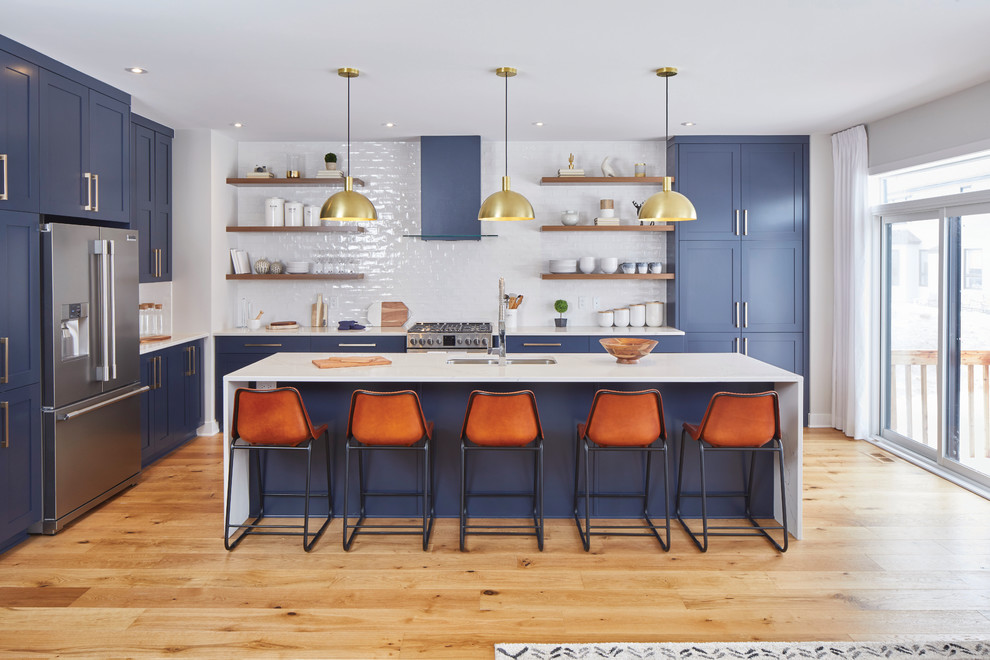 Mid-sized transitional l-shaped light wood floor and brown floor eat-in kitchen photo in Ottawa with an undermount sink, shaker cabinets, blue cabinets, white backsplash, ceramic backsplash, stainless steel appliances, an island and marble countertops