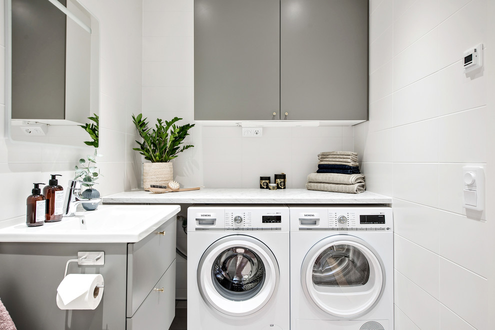 Design ideas for a small modern single-wall laundry room in Gothenburg with grey cabinets, marble benchtops and white walls.