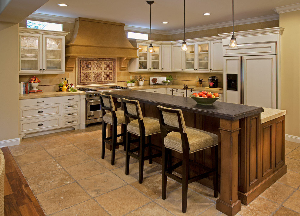 This is an example of a large mediterranean l-shaped open plan kitchen in Orange County with white cabinets, beige splashback, beige floor, limestone splashback, limestone floors, with island, a farmhouse sink, recessed-panel cabinets, limestone benchtops, stainless steel appliances and beige benchtop.
