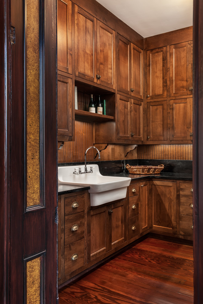 Photo of a large traditional l-shaped utility room in Other with a farmhouse sink, shaker cabinets, dark wood cabinets, solid surface benchtops, brown walls, a side-by-side washer and dryer, dark hardwood floors and brown floor.