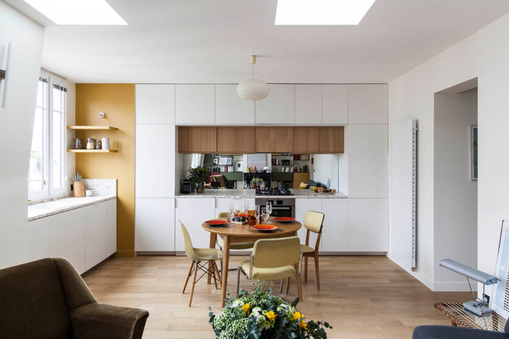 Photo of a contemporary l-shaped open plan kitchen in Paris with flat-panel cabinets, white cabinets, mirror splashback, stainless steel appliances, light hardwood floors, no island, beige floor and white benchtop.