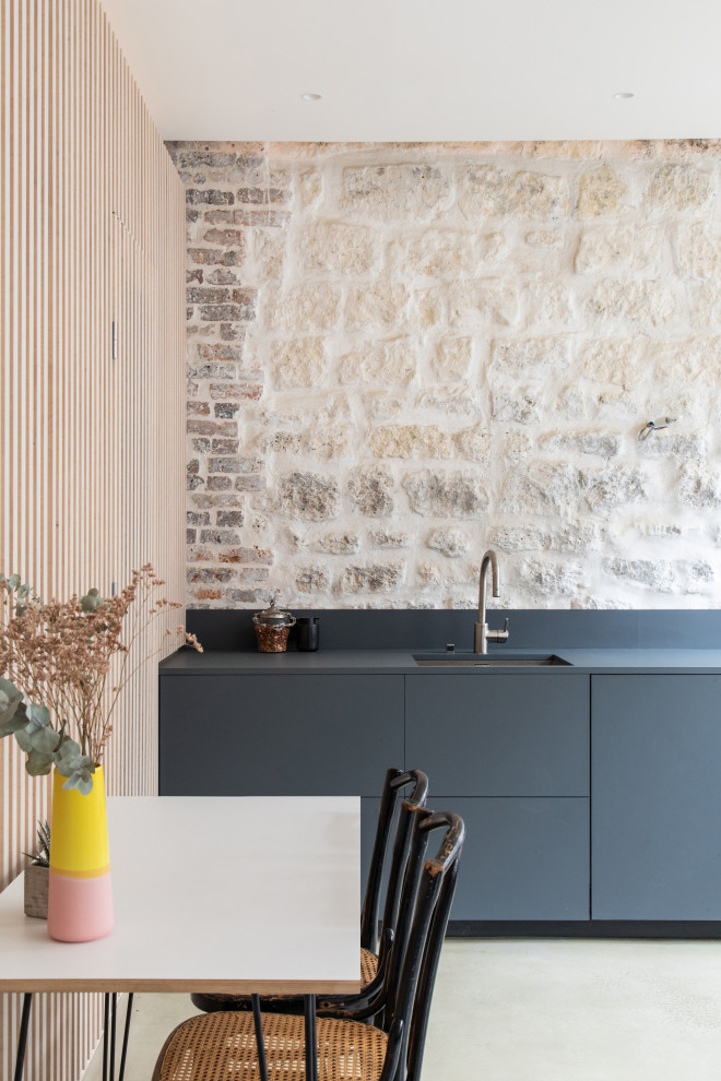 Photo of a small eclectic single-wall open plan kitchen in Paris with an undermount sink, beaded inset cabinets, grey cabinets, laminate benchtops, beige splashback, limestone splashback, stainless steel appliances, concrete floors, no island, grey floor and grey benchtop.
