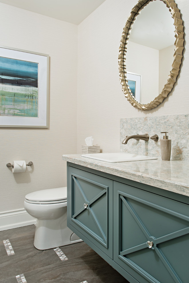 This is an example of a mid-sized transitional powder room in Toronto with blue cabinets, a two-piece toilet, brown tile, beige walls, porcelain floors, a drop-in sink, engineered quartz benchtops and beaded inset cabinets.