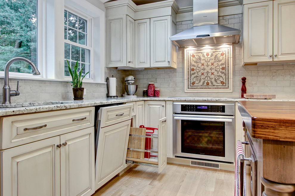 Example of a large transitional u-shaped light wood floor eat-in kitchen design in Boston with an undermount sink, raised-panel cabinets, distressed cabinets, granite countertops, beige backsplash, porcelain backsplash, stainless steel appliances and an island
