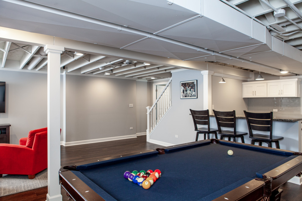 This is an example of a large transitional fully buried basement in Chicago with a game room, grey walls, vinyl floors, brown floor and exposed beam.
