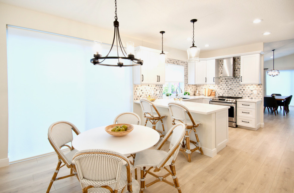 Small beach style u-shaped separate kitchen in Miami with an undermount sink, shaker cabinets, white cabinets, quartz benchtops, multi-coloured splashback, stone tile splashback, stainless steel appliances, laminate floors, a peninsula, beige floor and white benchtop.