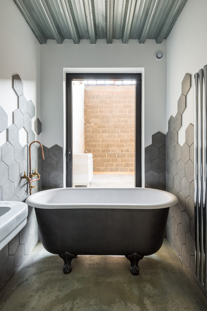 Small contemporary master bathroom in Lyon with a claw-foot tub, gray tile, white walls, concrete floors and a wall-mount sink.