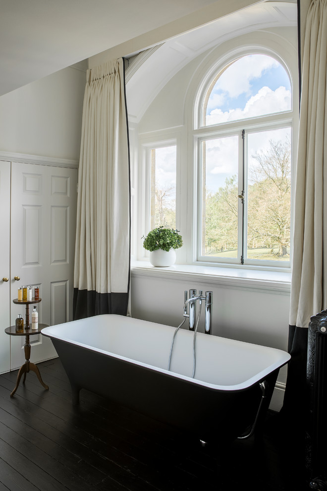 This is an example of a traditional master bathroom in London with a freestanding tub, white walls and dark hardwood floors.