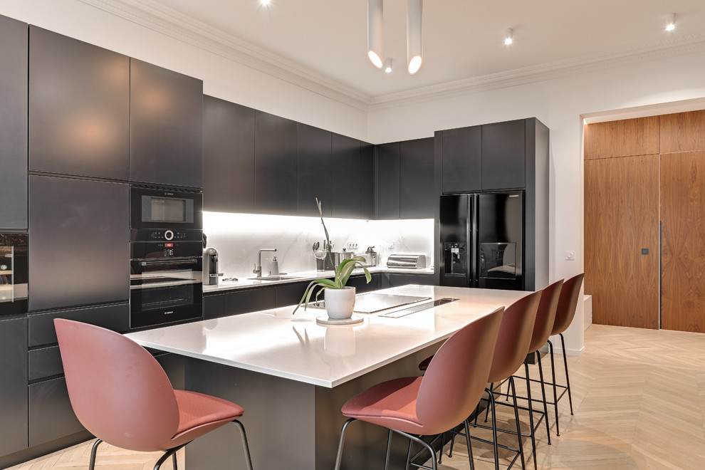 This is an example of a scandinavian l-shaped separate kitchen in Paris with a single-bowl sink, flat-panel cabinets, black cabinets, white splashback, black appliances, light hardwood floors, with island, beige floor and white benchtop.