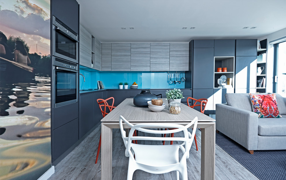 This is an example of a contemporary l-shaped kitchen in London with flat-panel cabinets, blue splashback, glass sheet splashback, light hardwood floors and stainless steel appliances.