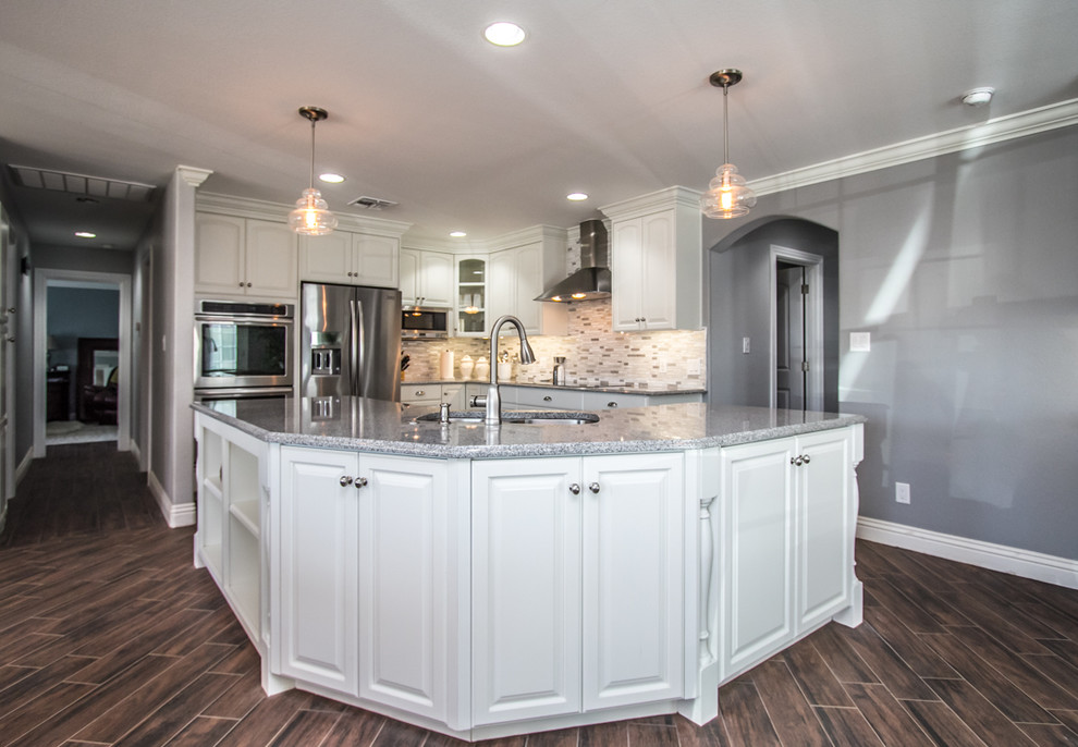 Example of a mid-sized transitional l-shaped dark wood floor and brown floor enclosed kitchen design in Phoenix with a double-bowl sink, raised-panel cabinets, white cabinets, multicolored backsplash, matchstick tile backsplash, stainless steel appliances and an island