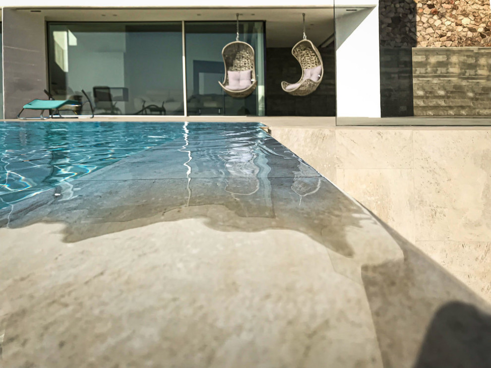 Mid-sized modern courtyard custom-shaped infinity pool in Madrid with a water feature and natural stone pavers.