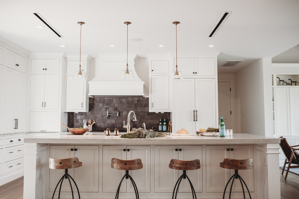 Design ideas for a large transitional l-shaped open plan kitchen in Austin with an undermount sink, shaker cabinets, white cabinets, quartzite benchtops, black splashback, slate splashback, panelled appliances, medium hardwood floors, with island, brown floor and beige benchtop.