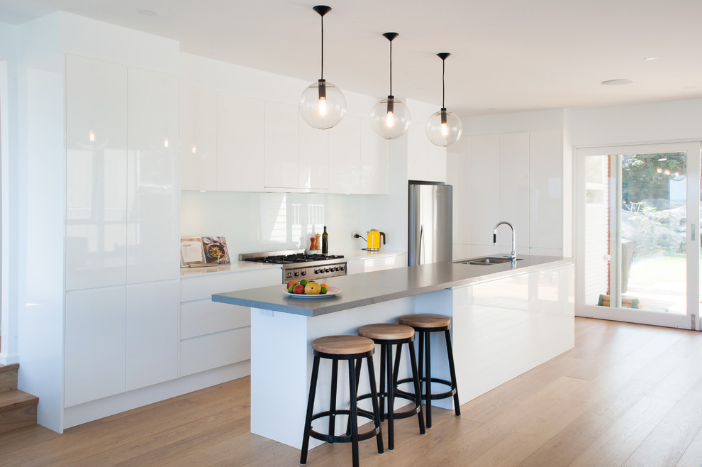 Inspiration for a contemporary galley kitchen in Sydney with a double-bowl sink, flat-panel cabinets, white cabinets, white splashback, stainless steel appliances, medium hardwood floors, with island, brown floor and white benchtop.