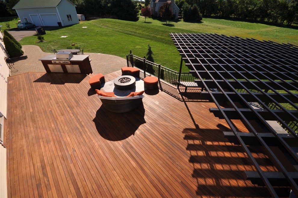 Example of a large transitional backyard deck design in New York with a fire pit and a pergola