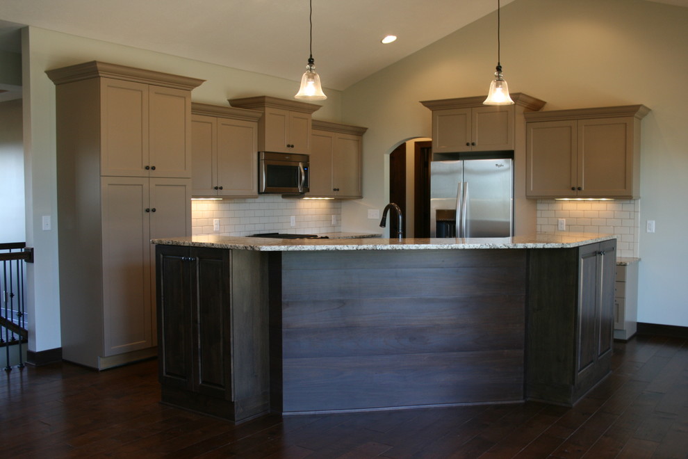 Inspiration for a mid-sized rustic l-shaped dark wood floor and brown floor open concept kitchen remodel in Omaha with an undermount sink, shaker cabinets, beige cabinets, granite countertops, white backsplash, subway tile backsplash, stainless steel appliances and an island