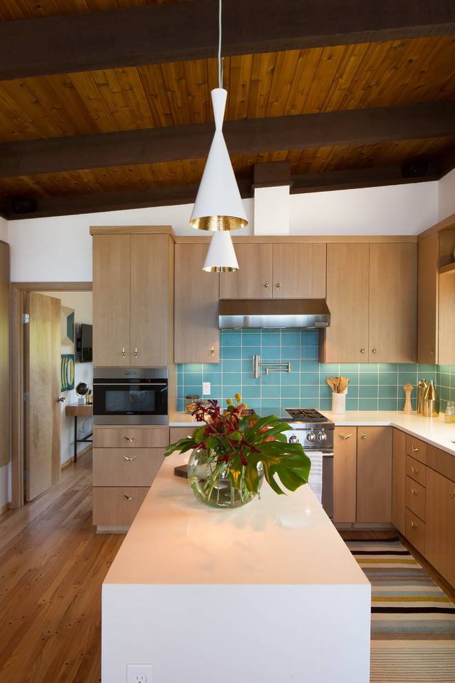 Photo of a mid-sized midcentury l-shaped separate kitchen in Seattle with flat-panel cabinets, medium wood cabinets, quartz benchtops, blue splashback, ceramic splashback, stainless steel appliances, medium hardwood floors, with island and brown floor.