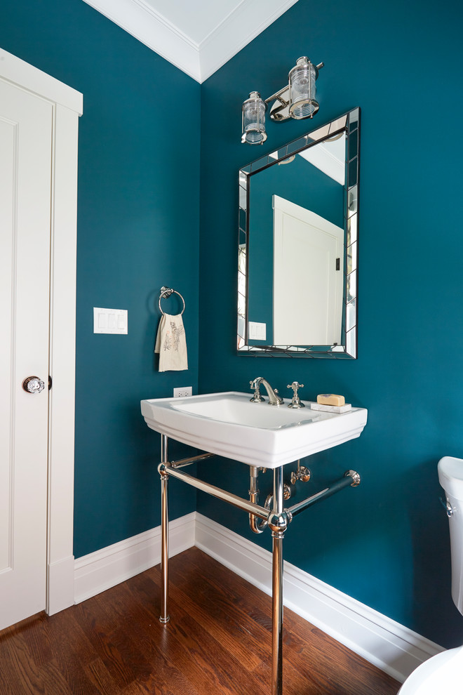Mid-sized traditional powder room in Chicago with blue walls, medium hardwood floors, a two-piece toilet, a wall-mount sink, solid surface benchtops, brown floor and white benchtops.