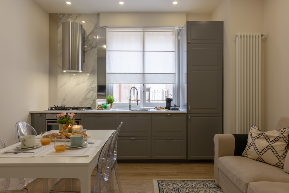 Photo of a small traditional single-wall open plan kitchen in Other with a drop-in sink, raised-panel cabinets, grey cabinets, laminate benchtops, multi-coloured splashback, window splashback, stainless steel appliances, light hardwood floors, no island, multi-coloured floor and white benchtop.