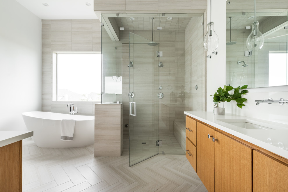 This is an example of a large contemporary master bathroom in Dallas with flat-panel cabinets, medium wood cabinets, a freestanding tub, a corner shower, white walls, ceramic floors, an undermount sink, engineered quartz benchtops, grey floor, a hinged shower door, white benchtops and gray tile.
