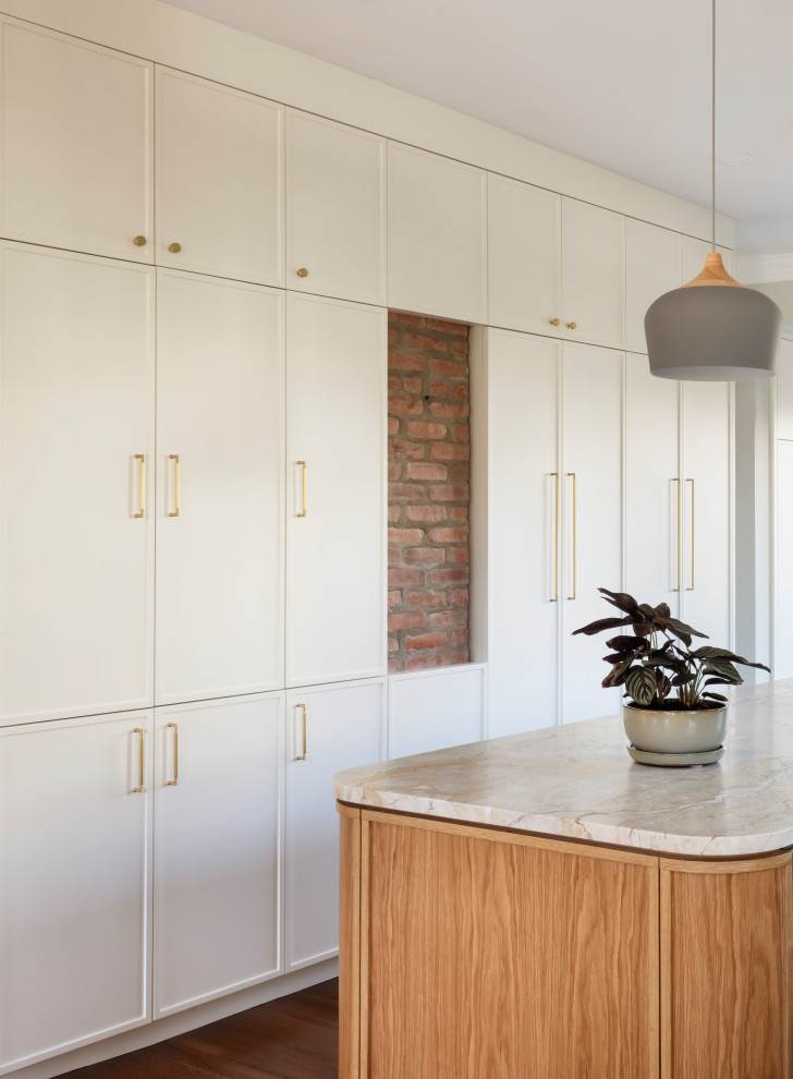 Inspiration for a medium tone wood floor eat-in kitchen remodel in Newark with white cabinets, quartzite countertops, an island, brick backsplash and paneled appliances