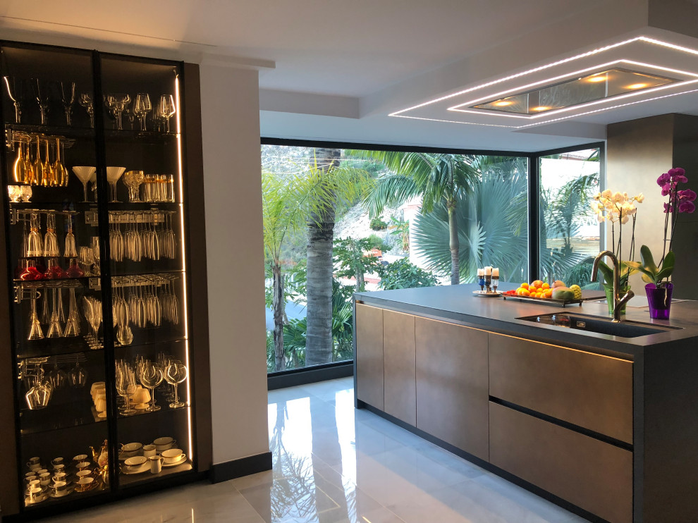 Inspiration for a large tropical u-shaped open plan kitchen in Malaga with a drop-in sink, flat-panel cabinets, distressed cabinets, tile benchtops, panelled appliances, marble floors, with island, white floor and black benchtop.